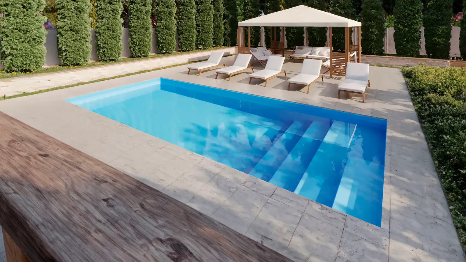 Piscina rectangular con deck de piedra clara, reposeras blancas y una cabaña, rodeada de cercos vivos altos