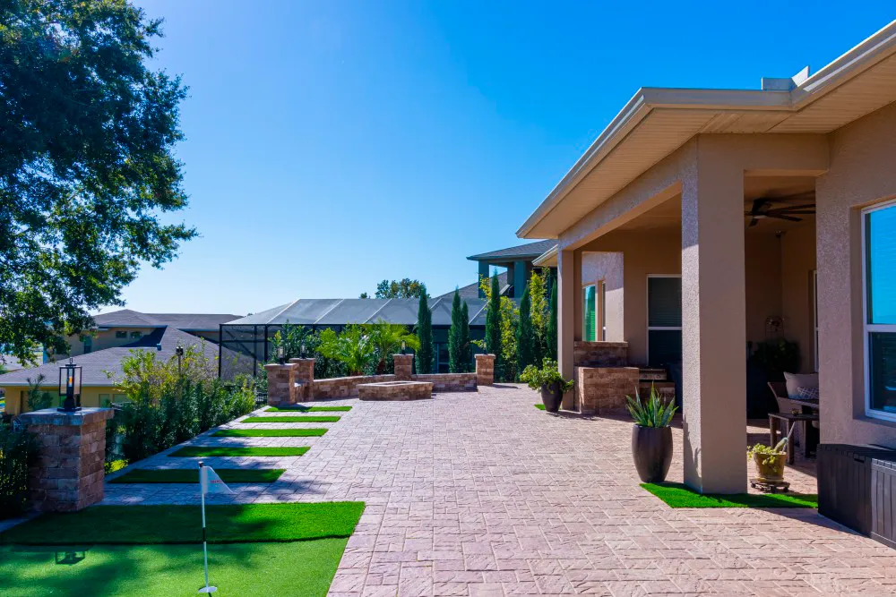Pátio de pavers tipo tijolo ao lado de uma casa na Flórida, com faixas de grama entre os pavers e um putting green